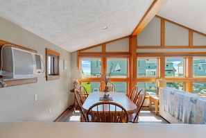 A dining area with a large table and chairs, a window with a view of houses, and a ceiling fan.