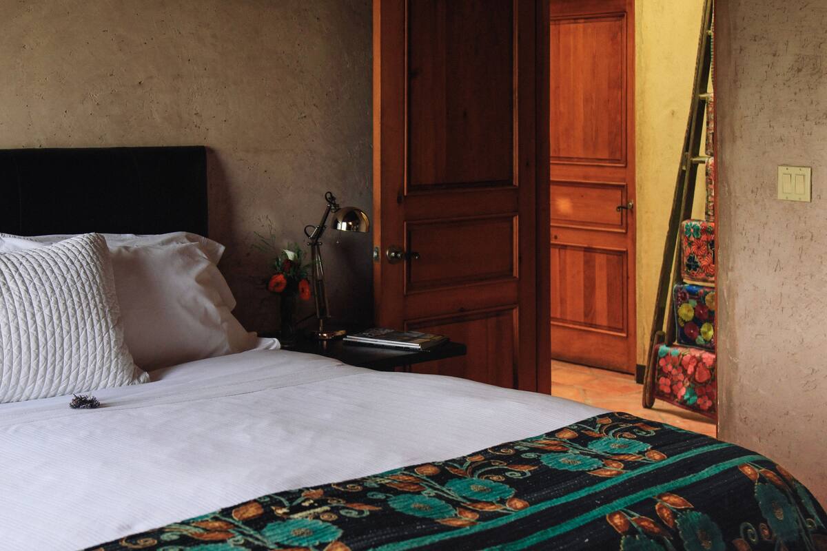 A bed with white bedding, a patterned throw, and a nightstand with a lamp and a book.