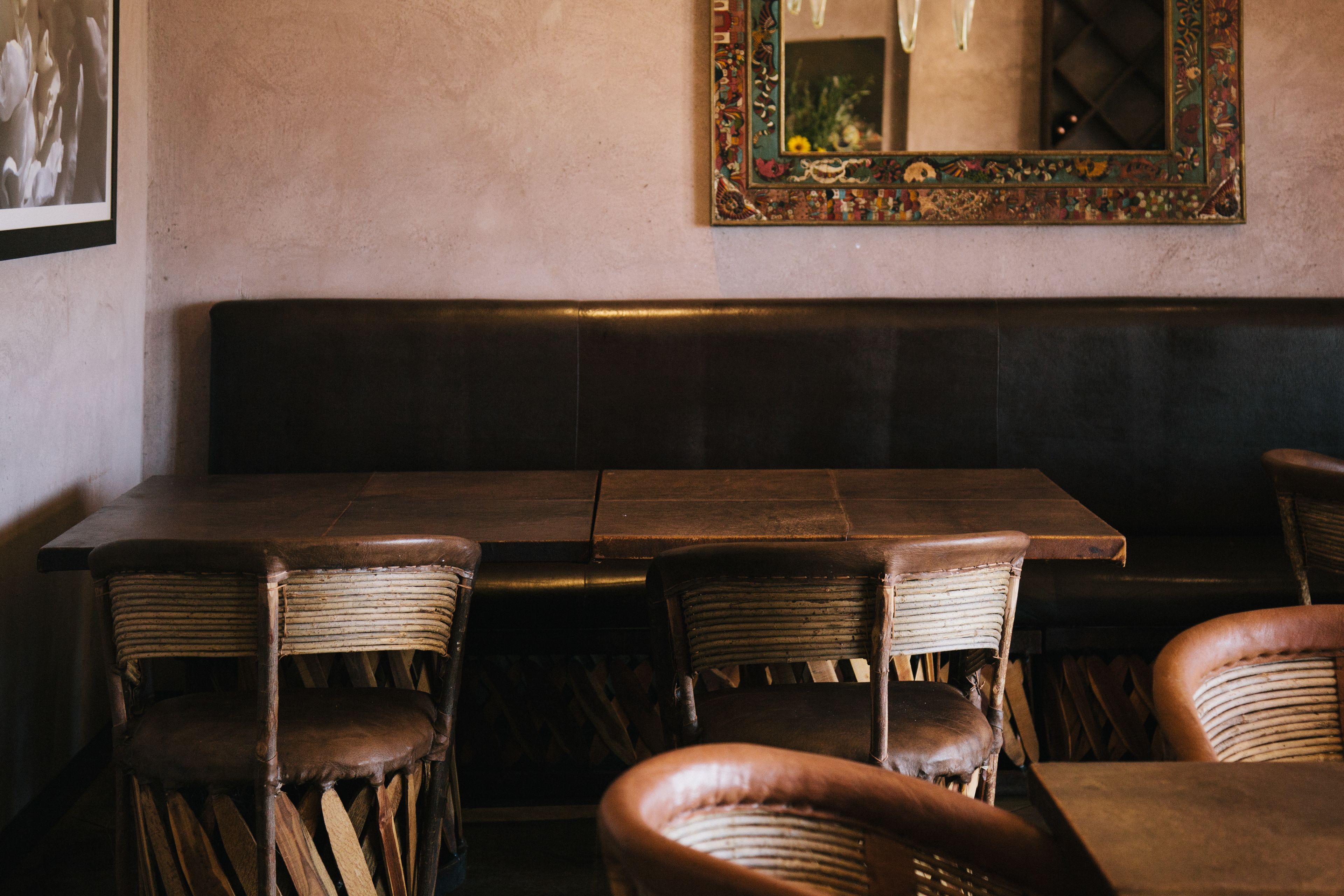 A restaurant interior with a long wooden table, wicker chairs, and a cushioned bench.
