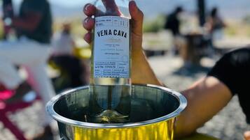 A hand holding a bottle of Vena Cava wine, placed in a metal bucket on a yellow table.