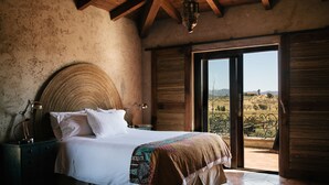 Un dormitorio con una cama grande, una mesita de noche, una lámpara y vistas al campo a través de una puerta corredera.