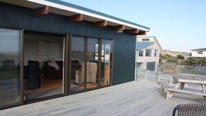 A modern building with a large sliding glass door leading to an interior space with furniture. - Comfortable Beach-Front House (Turakina Beach)
