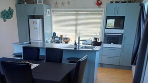 A compact kitchen with a central island, a dining area with a table and chairs, and a microwave oven. - Comfortable Beach-Front House (Turakina Beach)