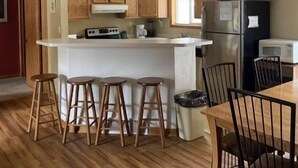 A kitchen with wooden cabinets, a central island with stools, a refrigerator, and a microwave. - Sunny Retreat at Springbrook Resort (Wisconsin Dells)
