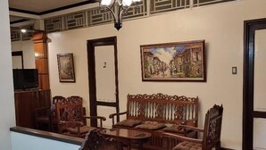 A room with a wooden floor, a ceiling light fixture, a sofa set, a television, and a framed picture on the wall. - Tops Lodging House (San Juan)