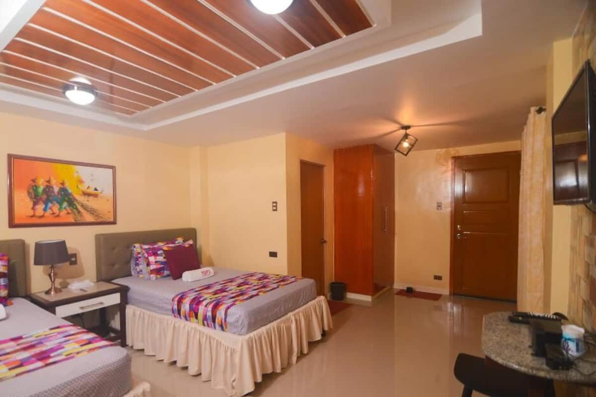 A hotel room with two beds, a desk, a chair, a TV, and a painting on the wall.