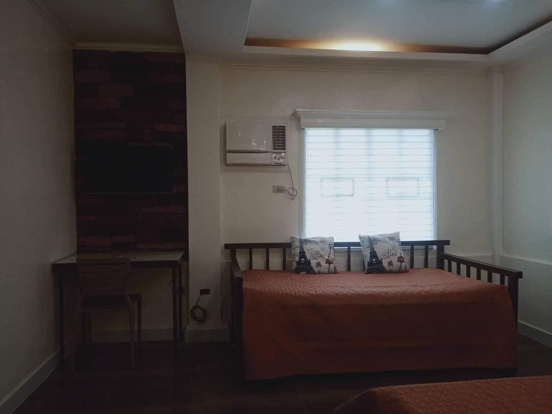 A bedroom with a bed, a desk, and a window with blinds.