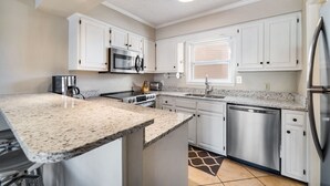 A modern kitchen with white cabinets, stainless steel appliances, granite countertops, and a tiled backsplash.