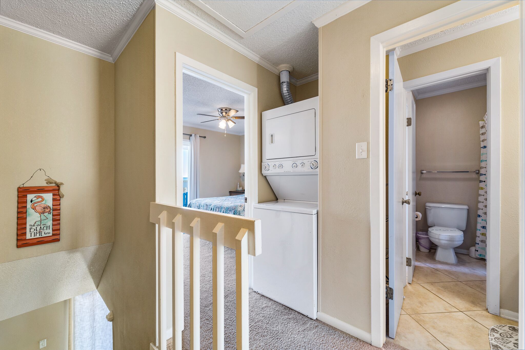 A hallway with a white door leading to a bathroom, a ceiling fan, and a wall-mounted heater.