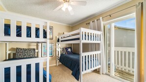 A bedroom with two bunk beds, a ceiling fan, and a large sliding glass door leading to a balcony.
