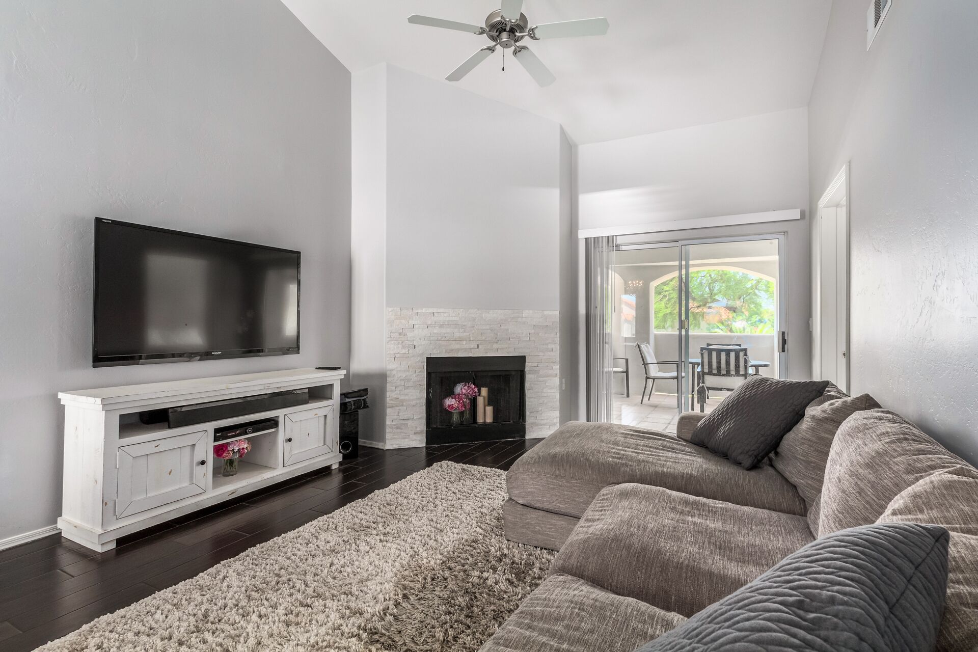A living room with a flat-screen TV, white entertainment unit, grey sofa, and a fireplace.