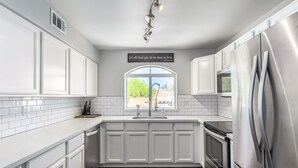 A modern kitchen with white cabinetry, a stainless steel refrigerator, a built-in oven, and a window with a view of greenery. - Picture Perfect Paradise Valley Condo (Paradise Valley)
