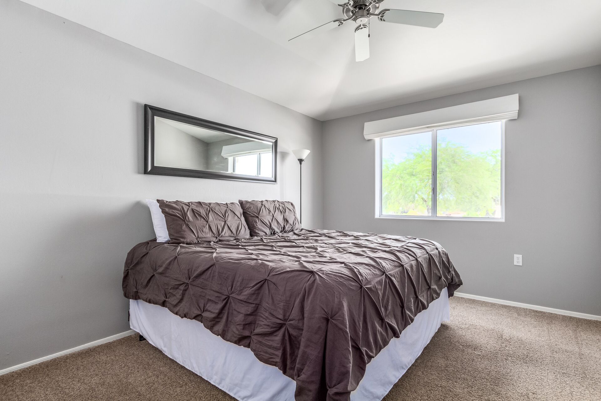 A bedroom with a bed, a ceiling fan, a window, and a mirror.