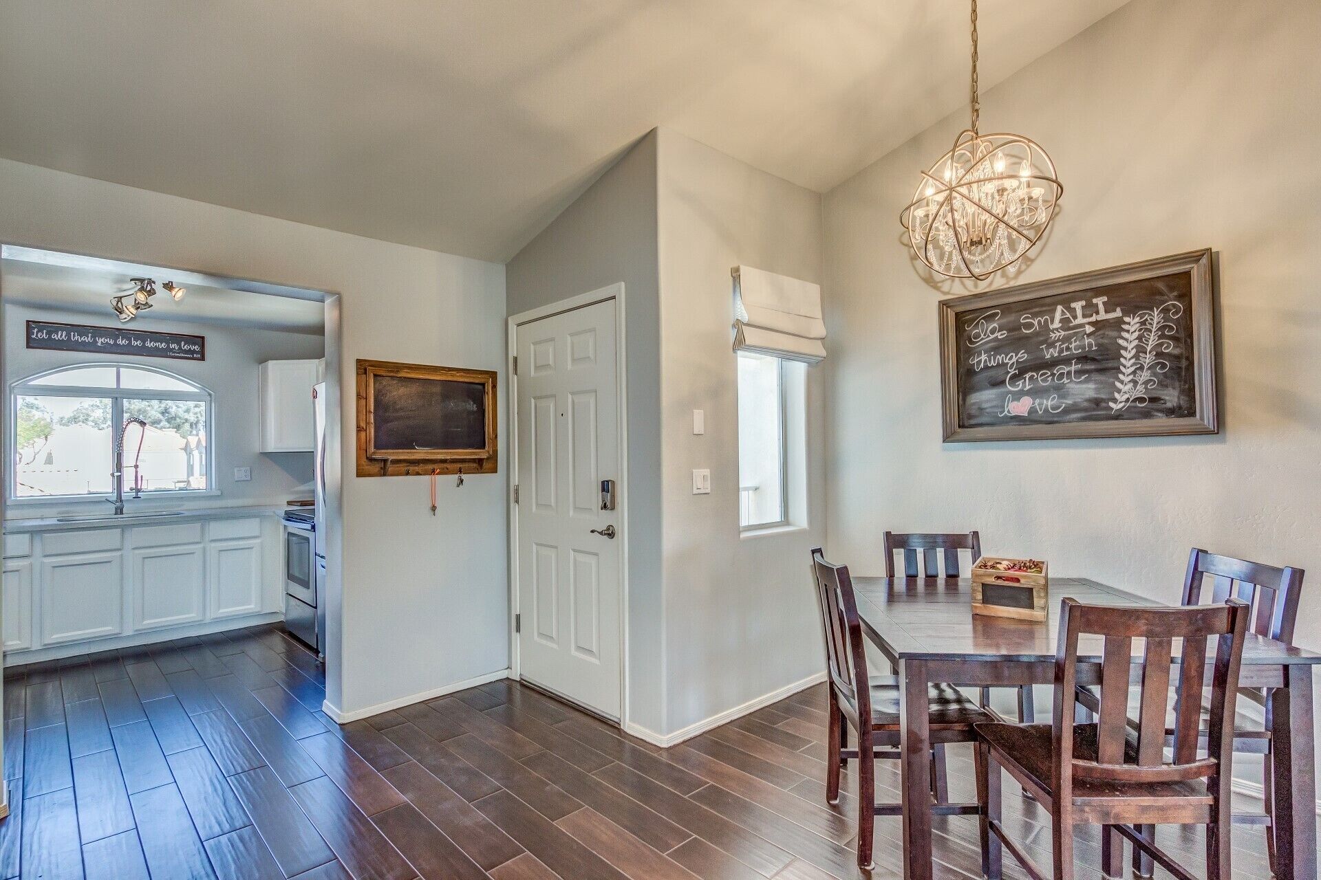 A dining area with a wooden table and chairs, a chandelier, and a chalkboard with a message.