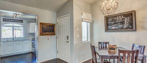 A dining area with a wooden table and chairs, a chandelier, and a chalkboard with a message.