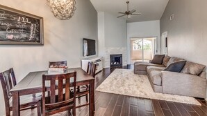 A living room with a fireplace, a ceiling fan, and a dining area with wooden chairs and a table. - Picture Perfect Paradise Valley Condo (Paradise Valley)