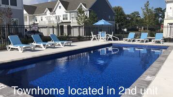 A swimming pool with lounge chairs and a fence. Text indicates a townhome is located in the second unit from the left of the building.