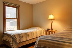 Una habitación pequeña y acogedora con dos camas individuales, una ventana y una mesita de noche con lámpara.