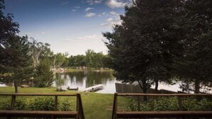 Une terrasse en bois avec des bancs donnant sur un lac, entourée d’arbres et d’une clôture en bois.