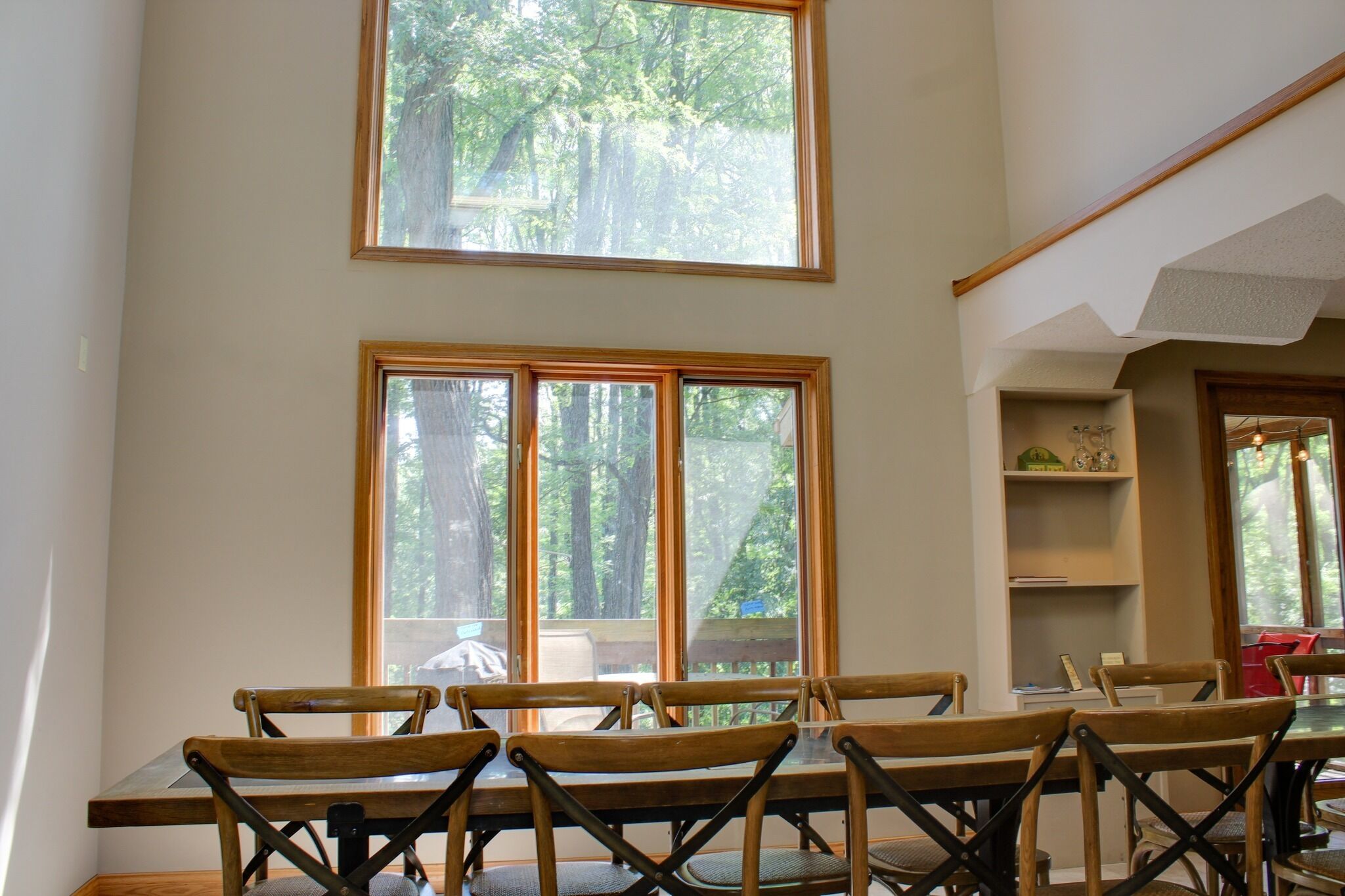 A dining area with a table and chairs, large windows with a forest view, and a shelf with decorative items.