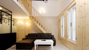 A modern living room with a wooden staircase, a black leather sofa, a white coffee table, and a wooden wall with a window. - Russo Hotel (Gangneung)