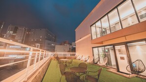 Eine Dachterrasse mit Sitzgelegenheiten im Freien und Blick auf die Skyline der Stadt im Abendrot.