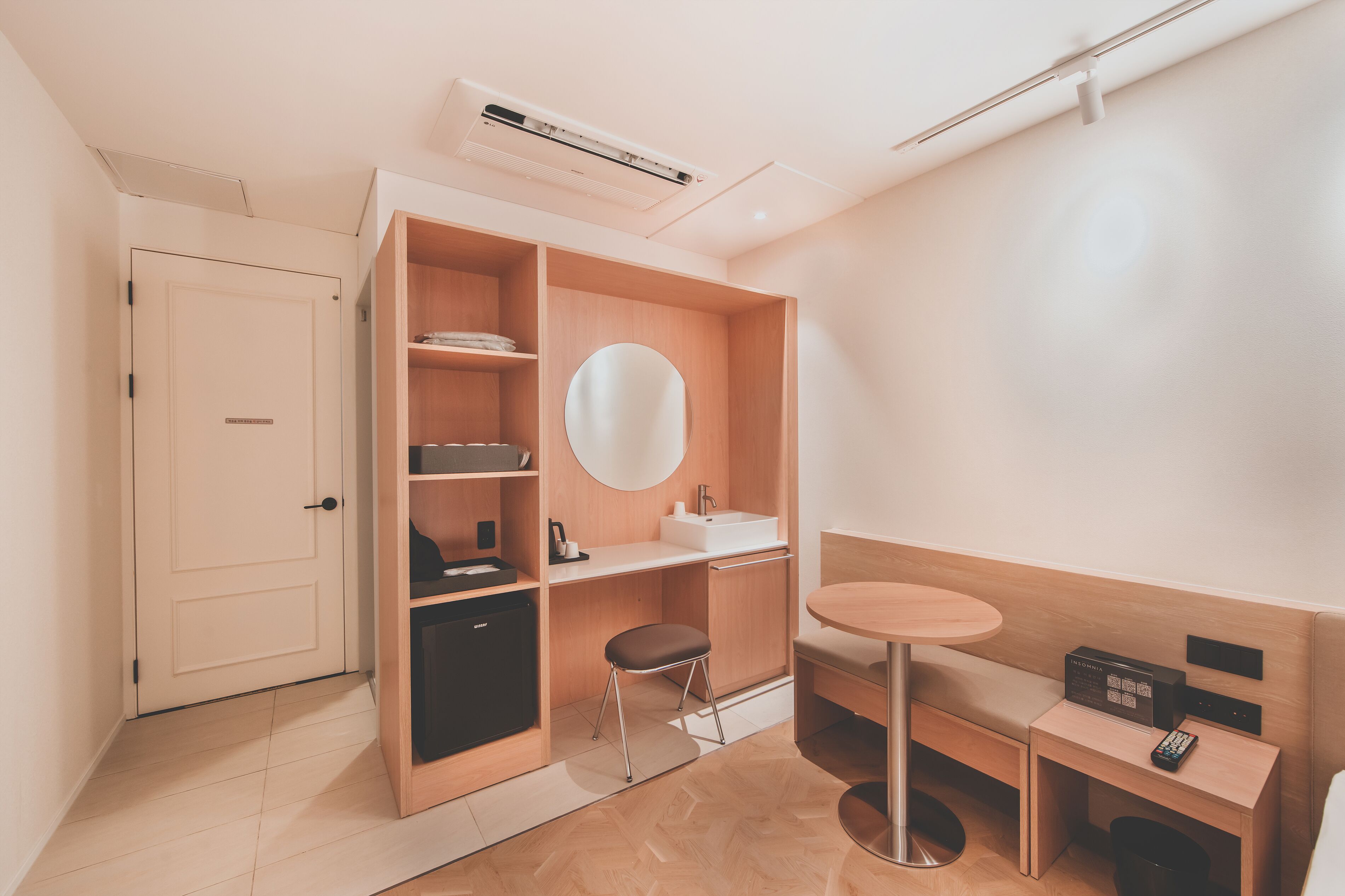 A compact hotel room with a wardrobe, a round mirror, a small table, and a bed.