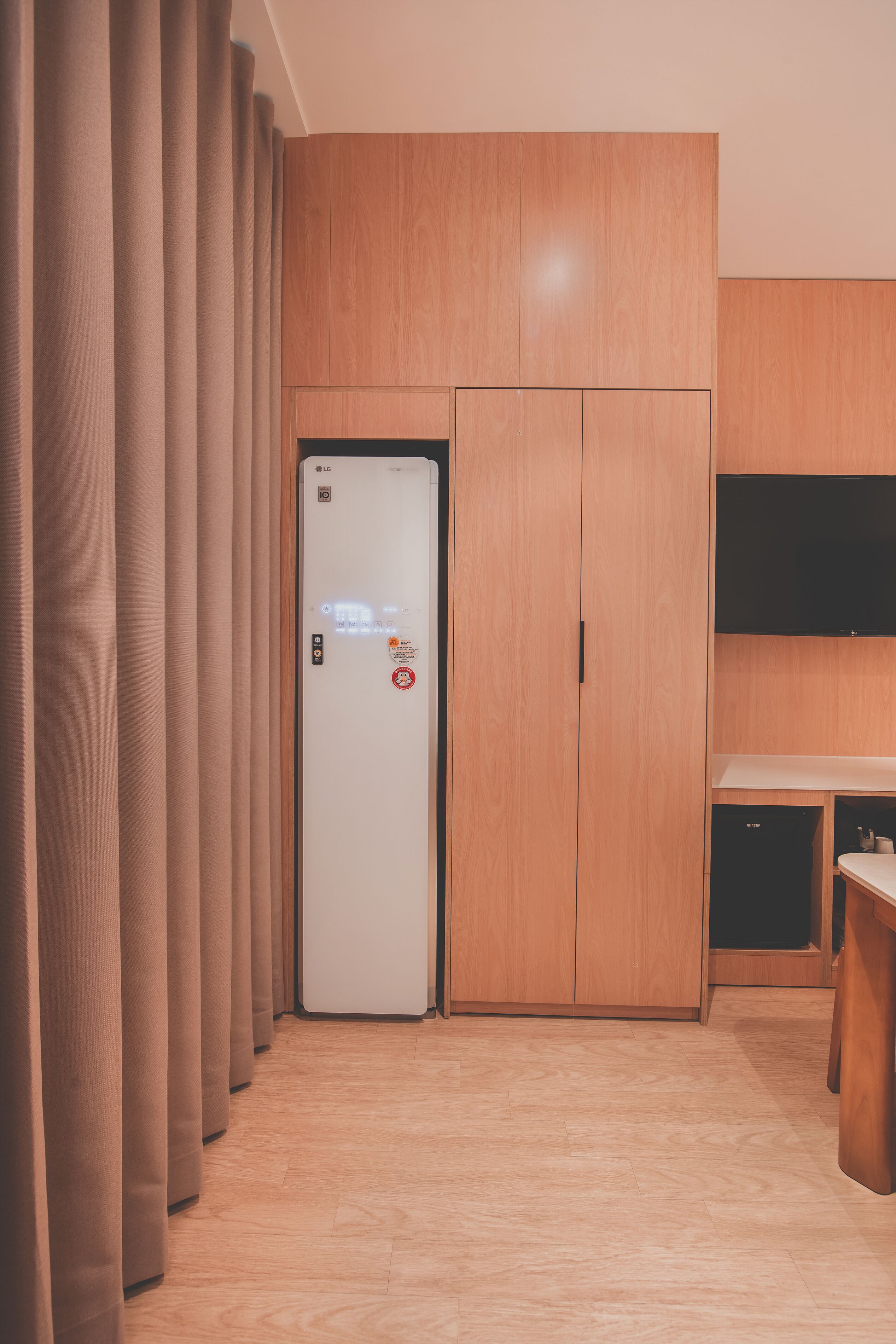 A hotel room with a wardrobe, a flat-screen TV, and a kitchenette.