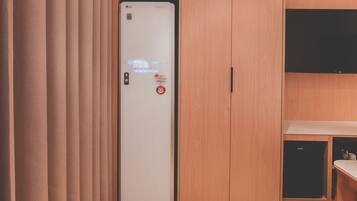 A hotel room with a wardrobe, a flat-screen TV, and a kitchenette.