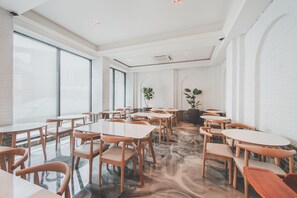 A spacious room with multiple tables and chairs, large windows, and a white brick wall. - Hotel Insomnia (Daegu)