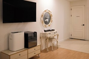 Ein Zimmer mit Flachbildfernseher, einer schwarzen Unterhaltungsecke, einem weißen Schminktisch mit Spiegel und einer Tür.