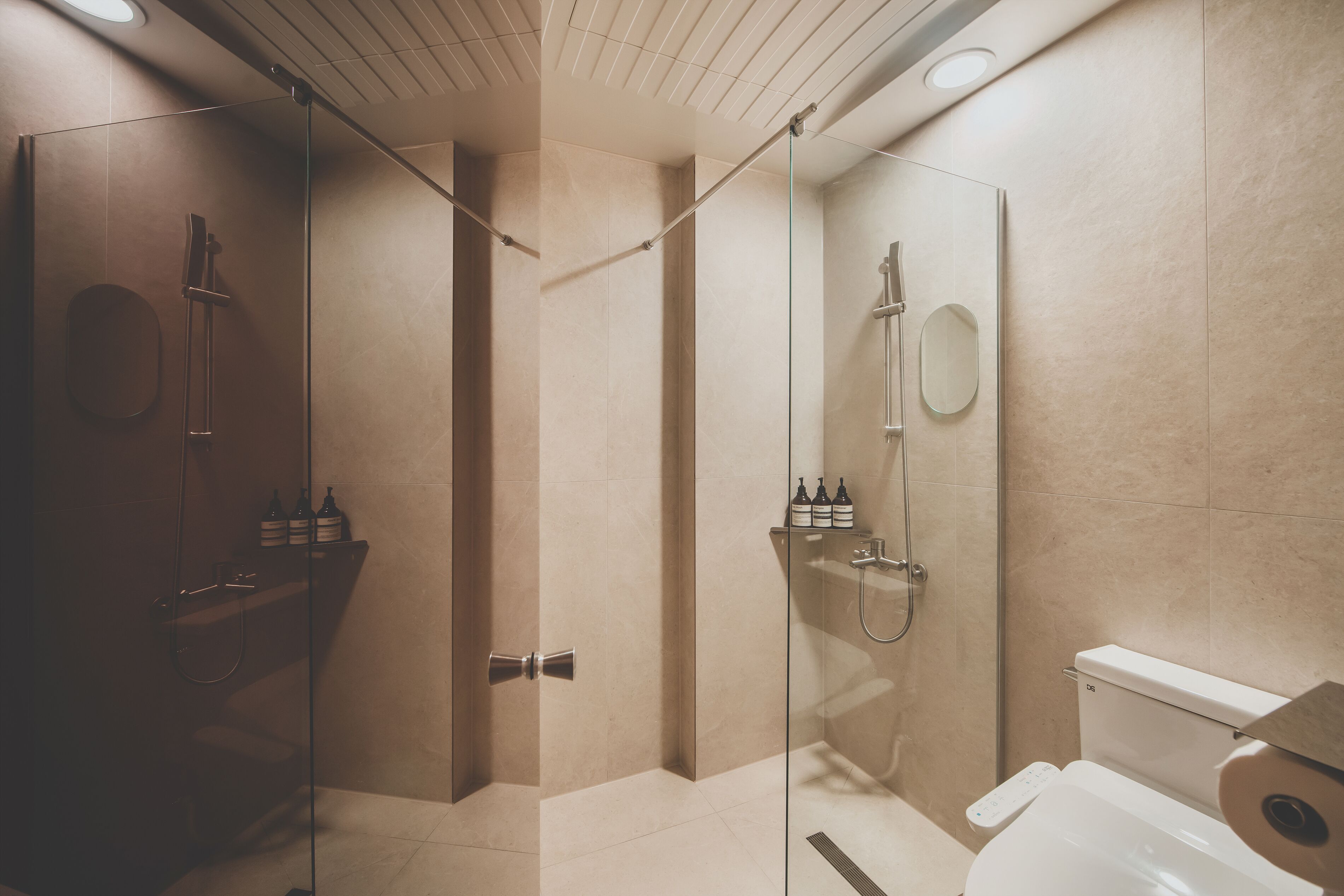 Un baño moderno con ducha de vidrio, inodoro y estante con artículos de aseo.