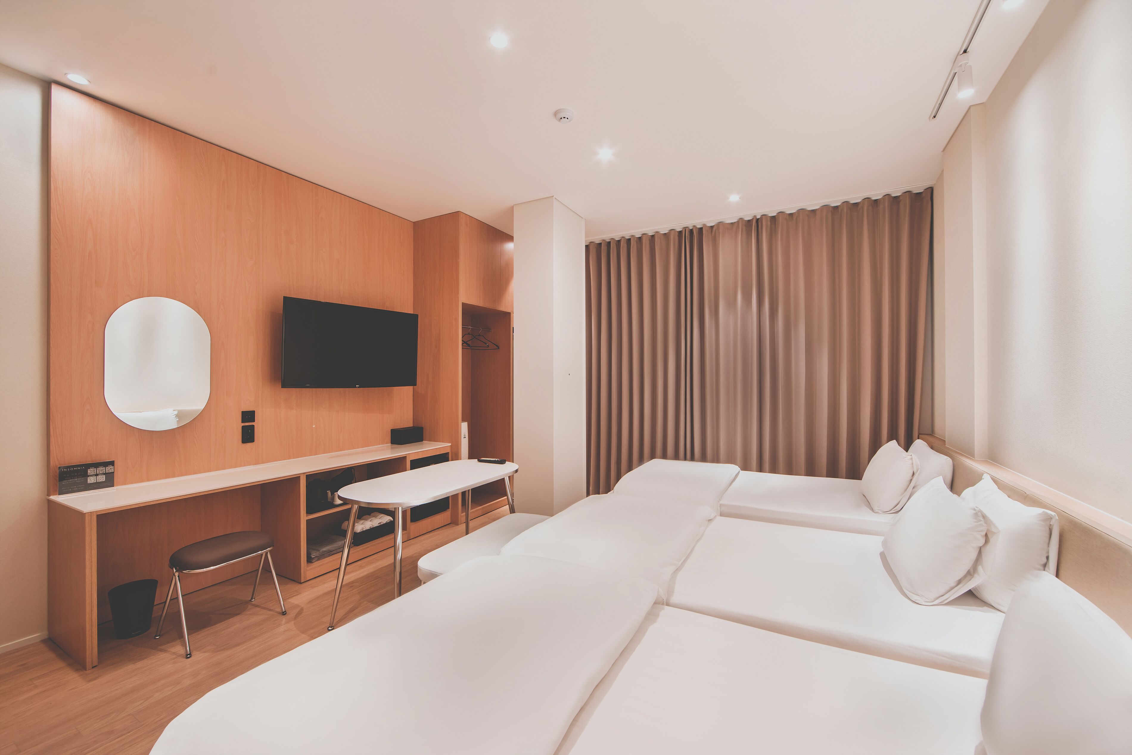 Moderni hotellihuone, jossa on suuri sänky, työpöytä tuolilla, seinälle asennettu taulutelevisio ja ikkuna, jossa on verhot.