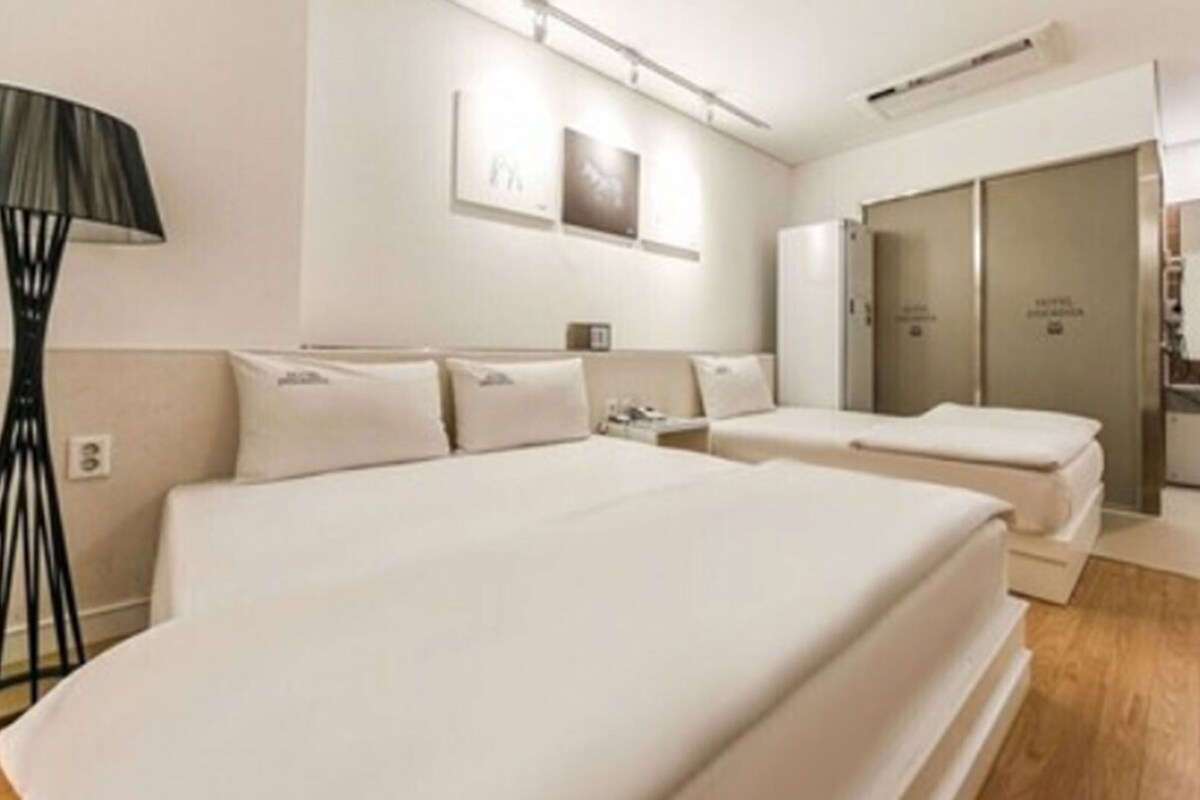 Une chambre d’hôtel avec deux lits, une table de chevet, une lampe, une armoire et une salle de bain avec un miroir.