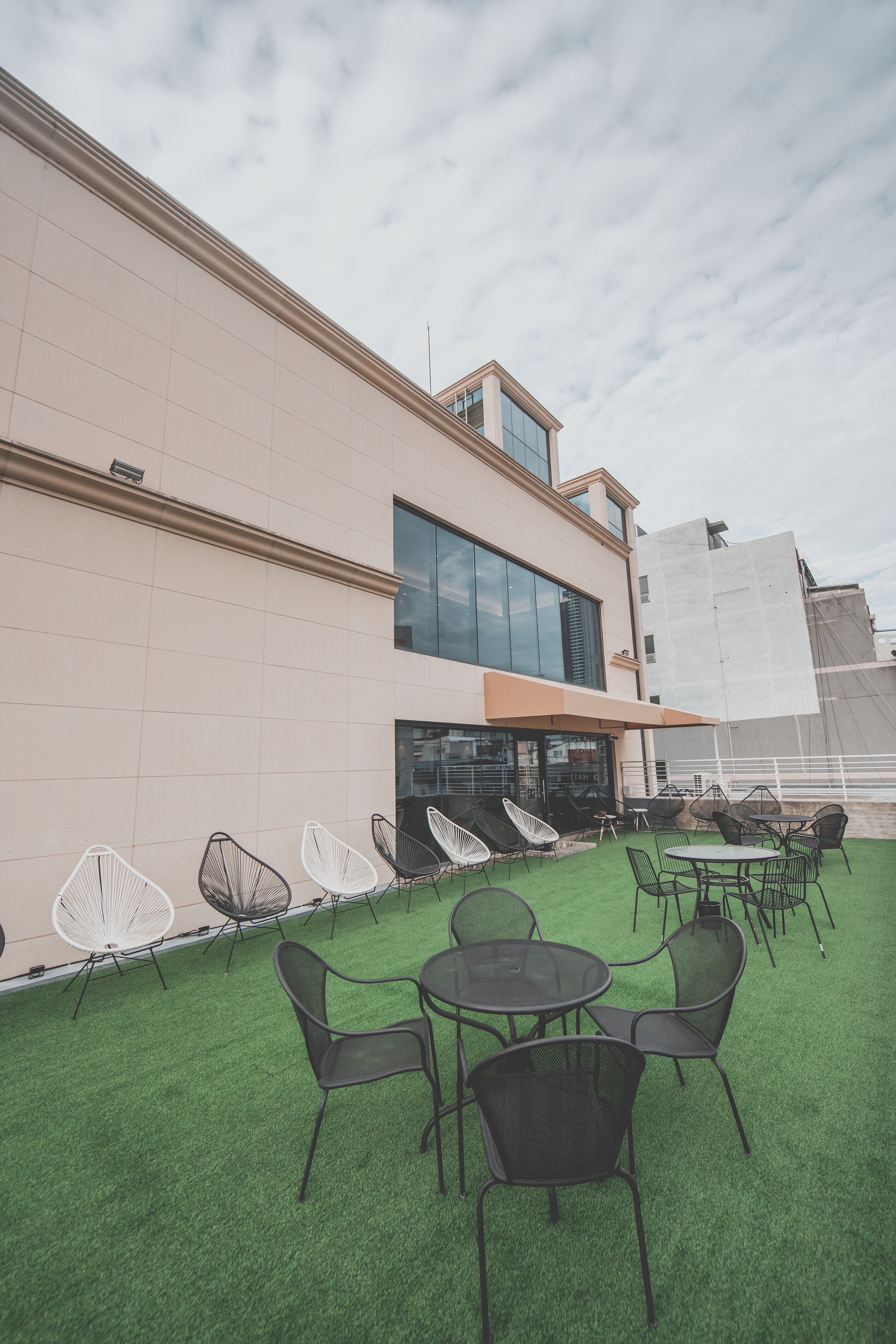 An outdoor seating area with chairs and tables, a building with a flat facade, and a clear sky.