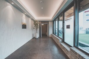Un pasillo de diseño moderno, con una planta en maceta, un aplique en la pared y una puerta de cristal que da a un espacio exterior.