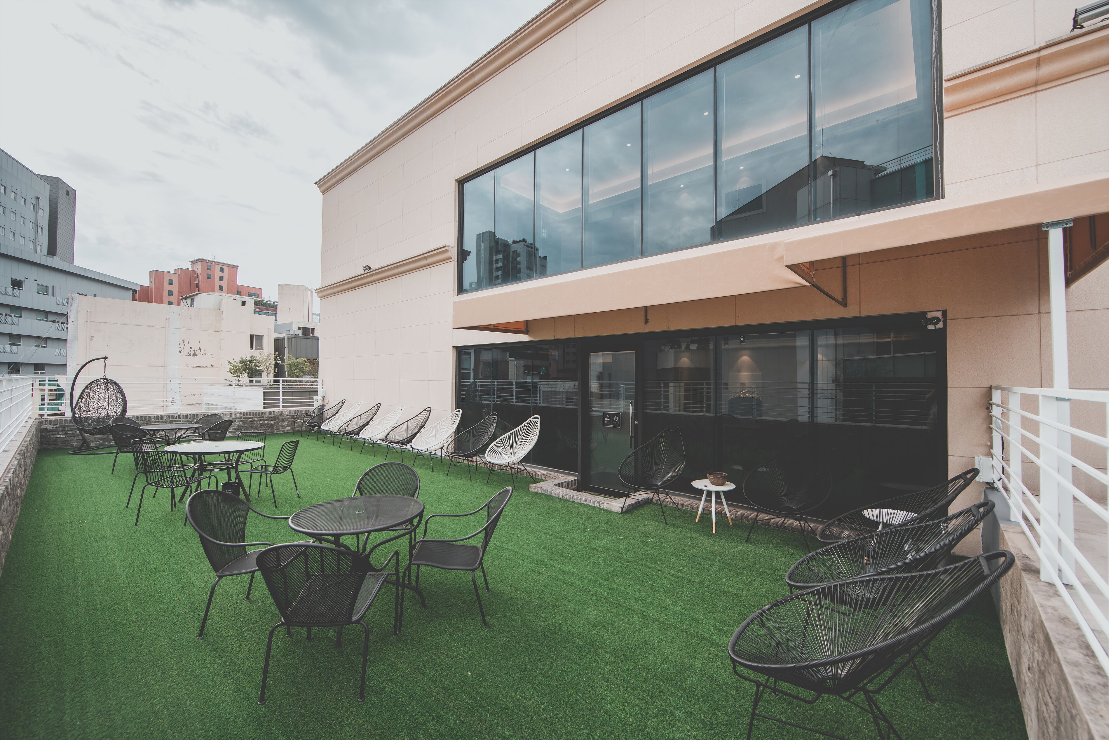 Terraza en la azotea con césped artificial, mobiliario exterior y un edificio con fachada de vidrio.