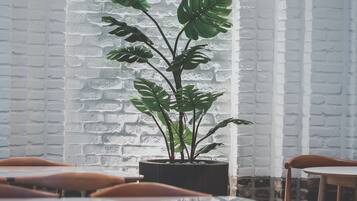 Interior de restaurante con paredes de ladrillo blanco, una planta grande en el centro y mesas y sillas de madera.