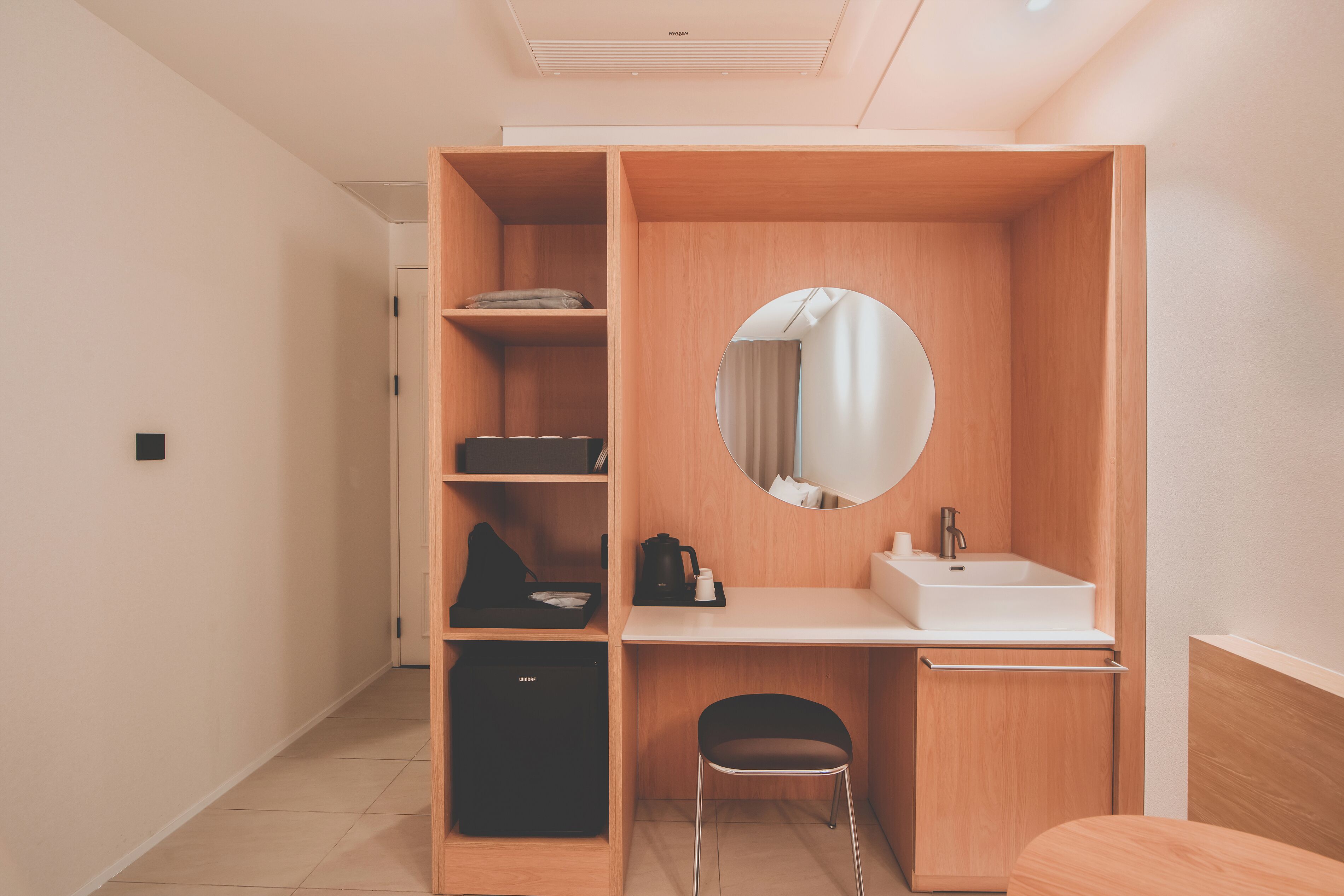 A compact hotel room with a built-in wardrobe, a small sink, and a mirror.