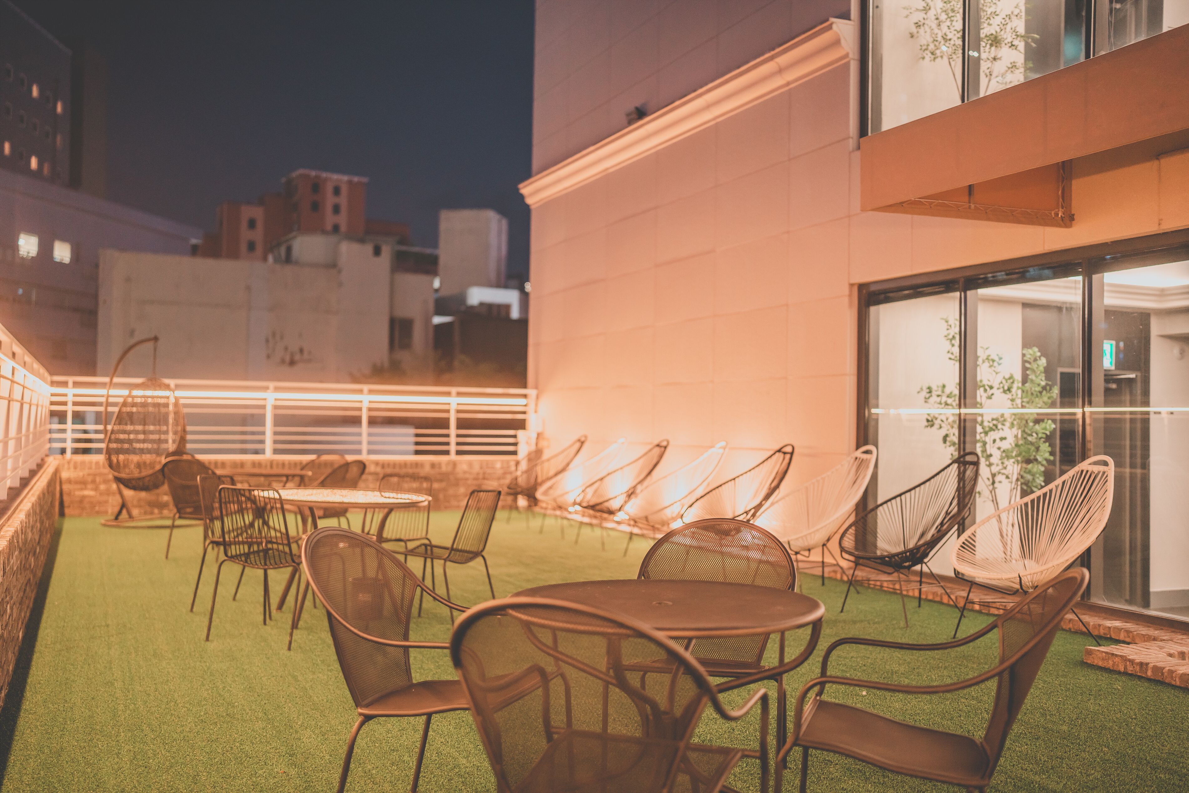 An outdoor seating area with tables and chairs, a glass door leading inside, and a view of the cityscape in the background.