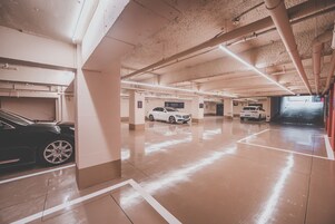 A multi-level parking garage with white walls and concrete floors, featuring several parked cars and visible structural elements like columns and pipes.