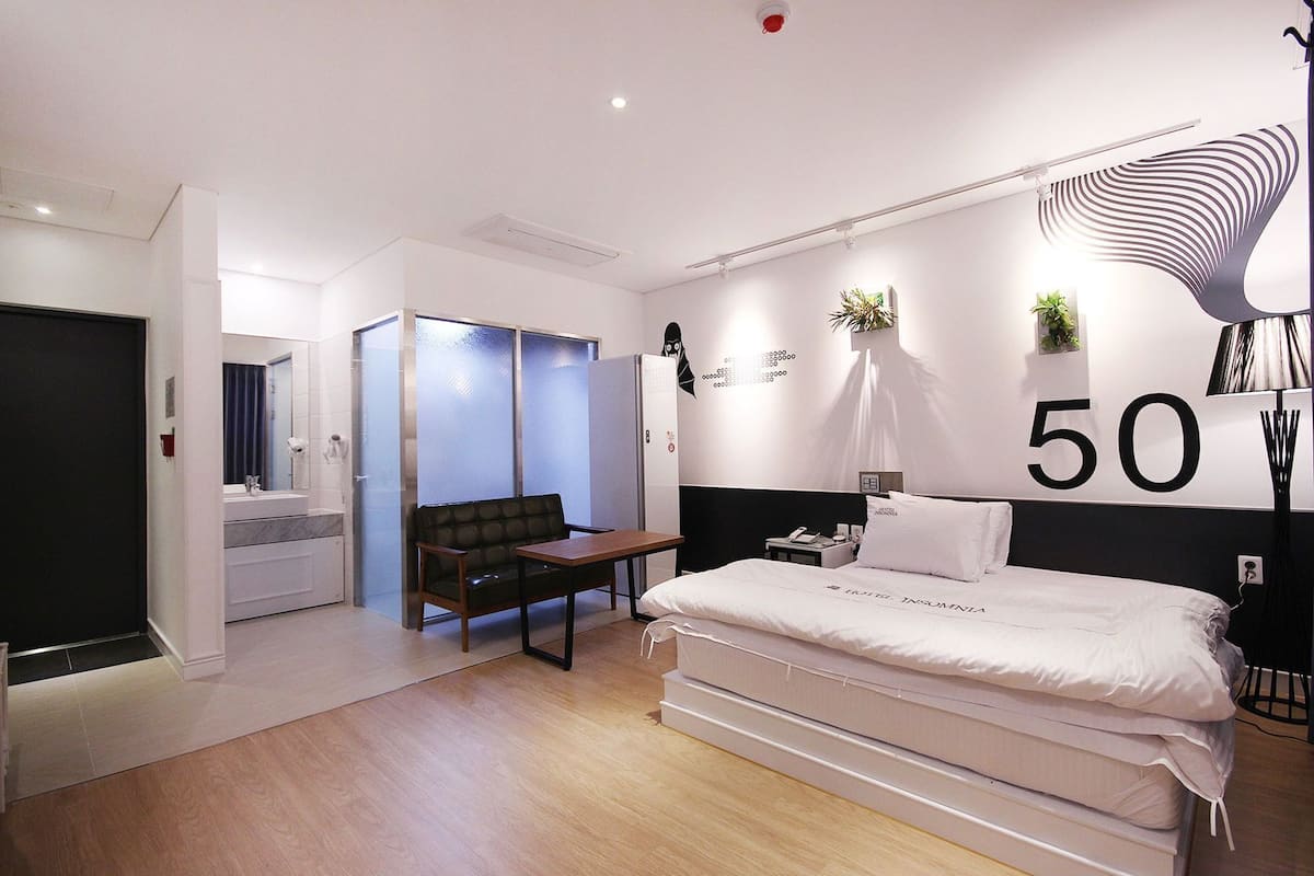 Una habitación de hotel moderna con una cama grande, un escritorio, una silla, una mesita, un espejo y el número 50 en la pared.