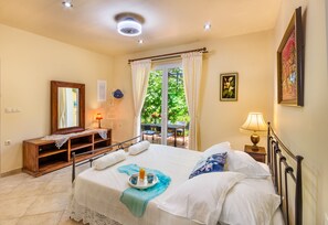 A bedroom with a bed, bedside table, lamp, and a view of the outdoors.