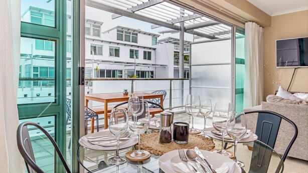 A dining area with a glass table set for four, a sofa, and a TV on the wall.