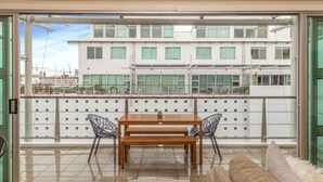 A balcony with a wooden table and chairs, a sofa, and a view of a white building with multiple windows.