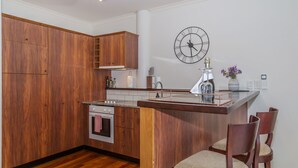 A modern kitchen with wooden cabinets, a built-in oven, and a dining area with two chairs.