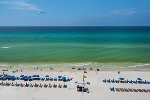 Ein Strand mit Reihen von Liegestühlen und Sonnenschirmen, einem Rettungsturm und freiem Blick auf das Meer.