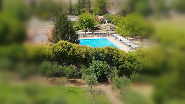 A swimming pool surrounded by greenery, with a covered seating area and a building in the background. - holiday home IL GIRASOLE (Castel Ritaldi)