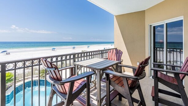 Un balcón con vista a la playa, una piscina y una mesa con sillas.