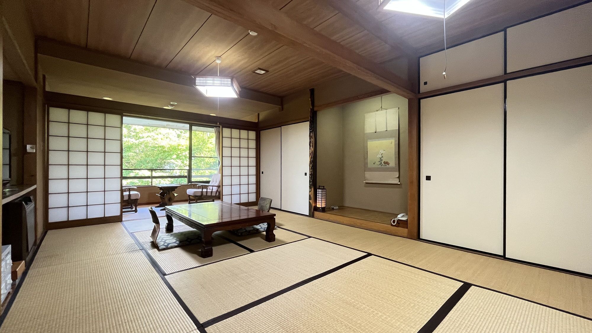 A traditional Japanese room with tatami flooring, a low wooden table, sliding doors, and a view of greenery outside.